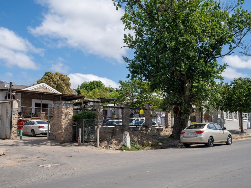 Street view of the commercial property featuring a stone boundary wall, metal security fencing, and mature landscaping along the roadside.