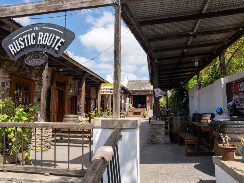A rustic outdoor commercial courtyard featuring stone walls, timber pergola roofing, and paved walkways, providing an inviting open-air seating area.