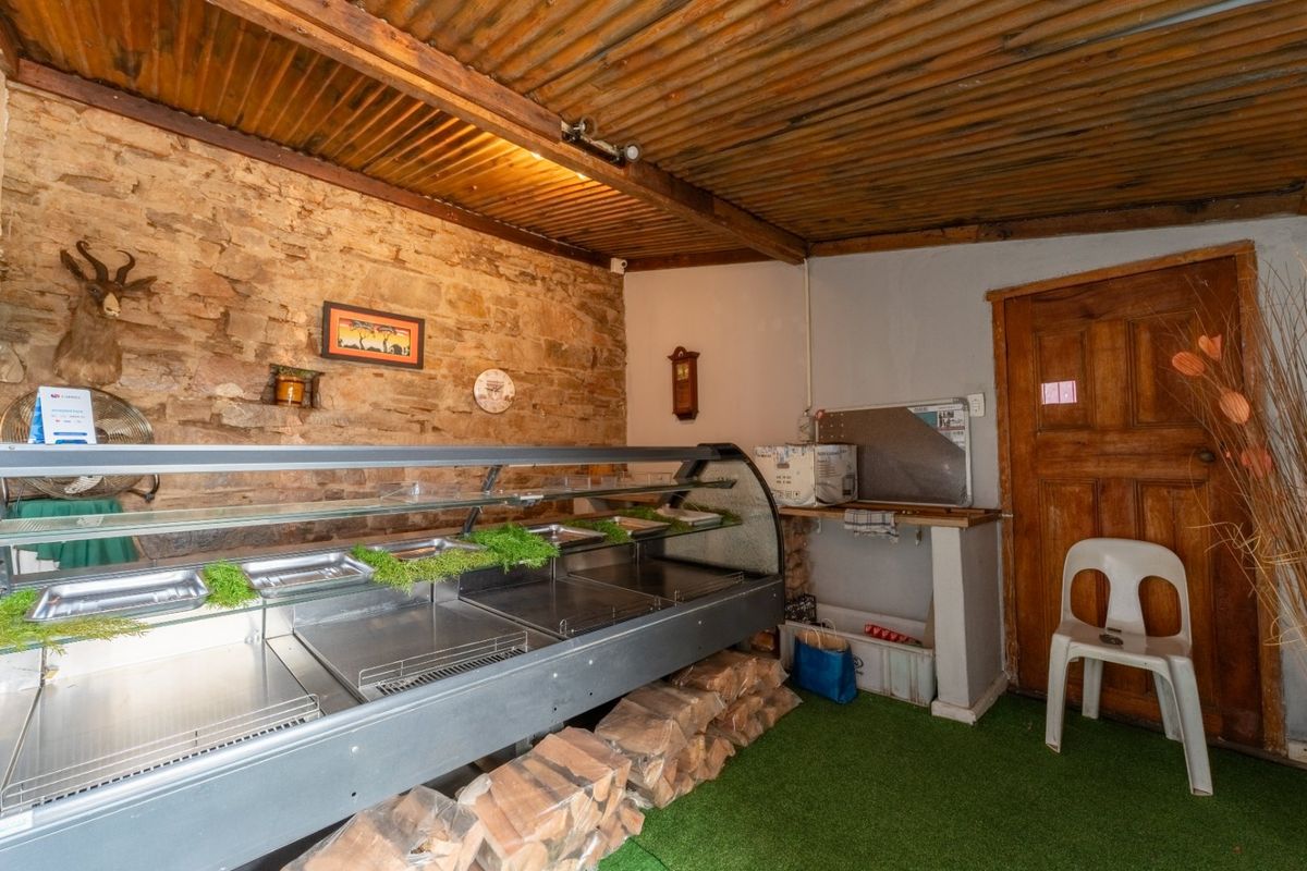 A rustic commercial food preparation or display area featuring an exposed stone wall, corrugated metal ceiling, and a built-in refrigerated display counter.