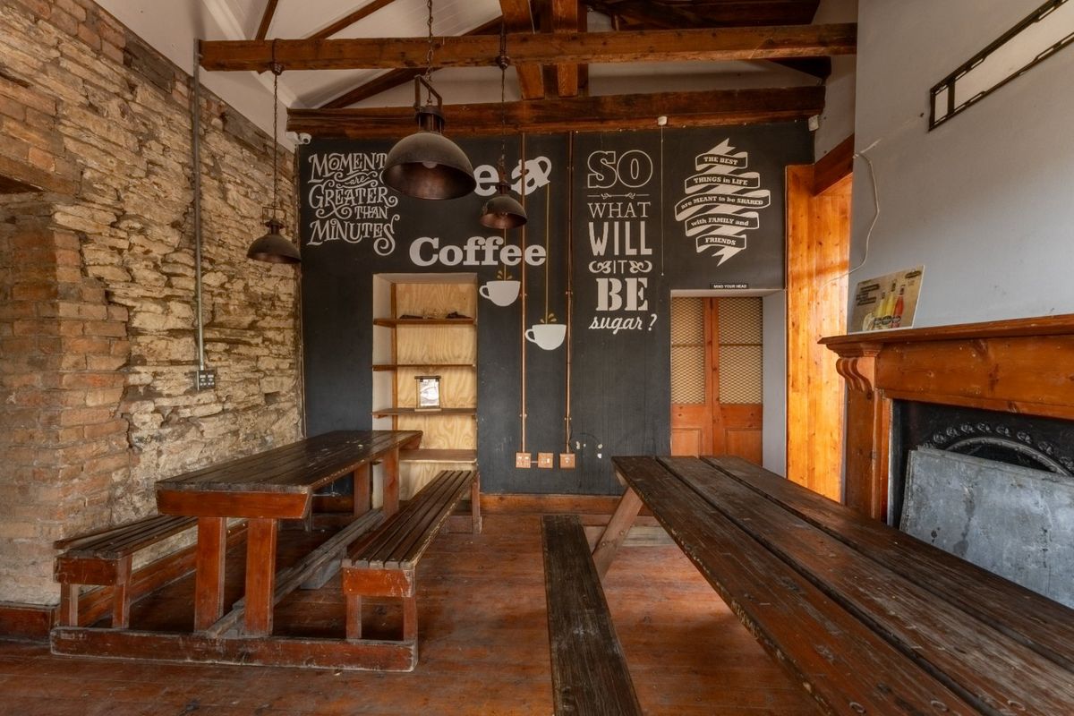 Rustic commercial interior featuring exposed brick walls, timber ceiling beams, hardwood flooring, and a traditional fireplace, creating a warm and characterful atmosphere.