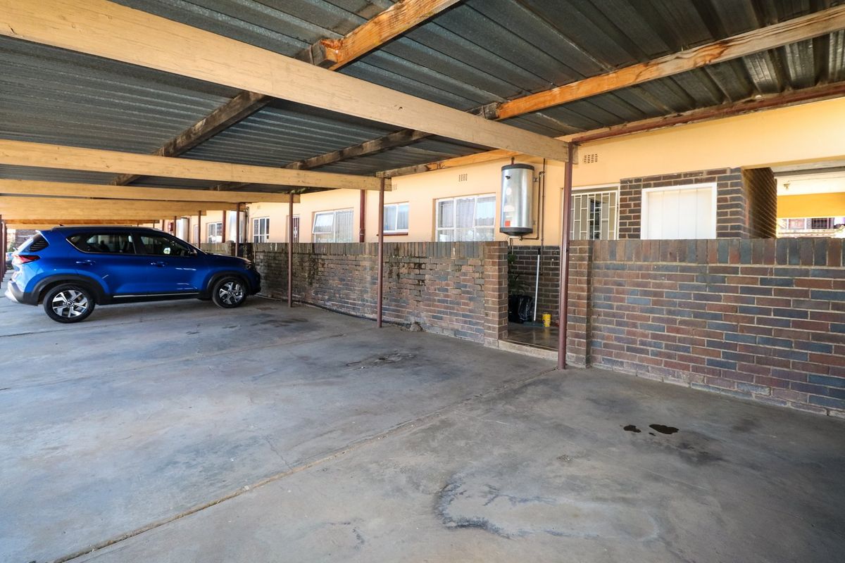 Covered carport area featuring a corrugated metal roof, brick boundary walls, and an external wall-mounted electric water heater.