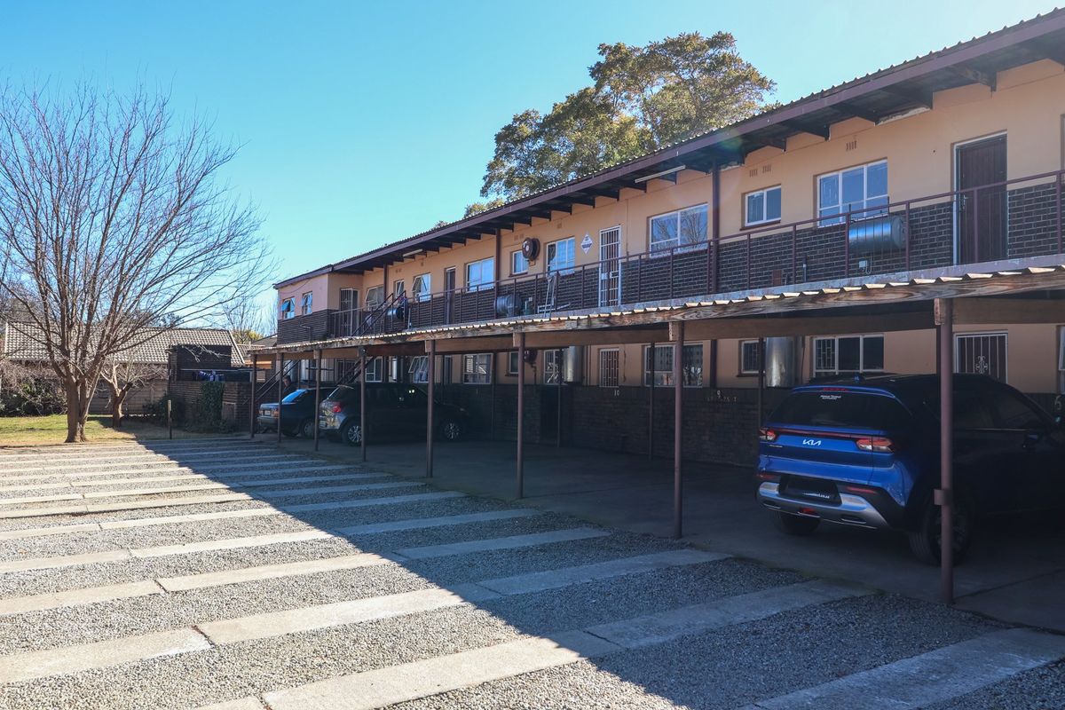 Exterior view of an apartment complex featuring covered parking bays, metal balcony railings, and a multi-level residential facade.