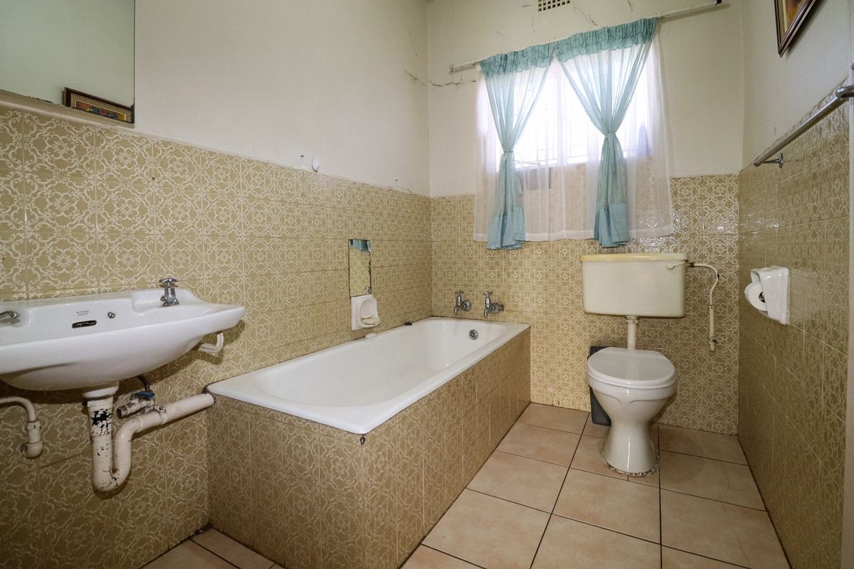 A dated bathroom featuring a bathtub, pedestal basin, and toilet, finished with vintage patterned wall tiles and ceramic floor tiling.