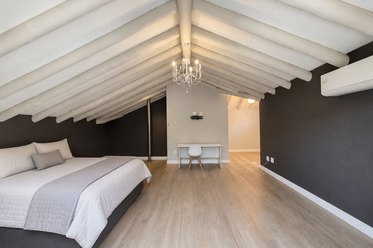 Spacious bedroom featuring a vaulted ceiling with exposed timber beams, laminate flooring, and a wall-mounted air conditioning unit.