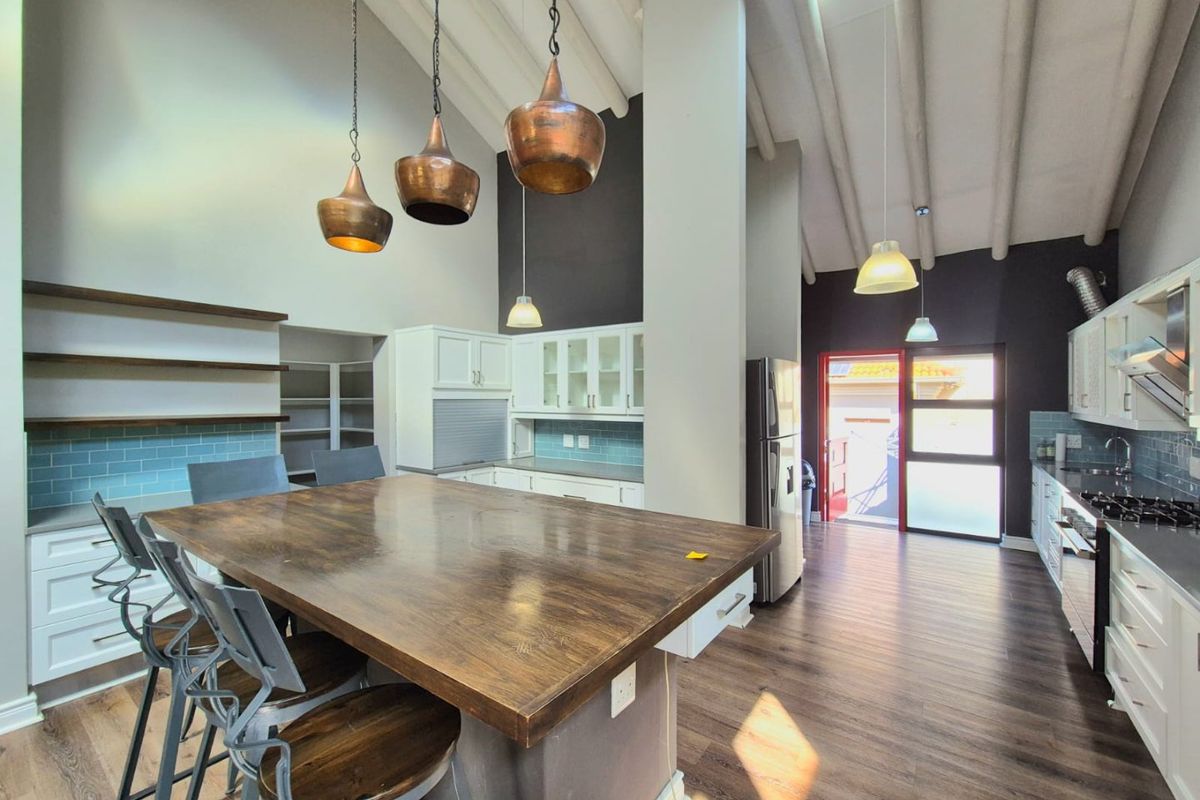 Spacious modern kitchen featuring a large central island, exposed timber ceiling beams, skylight, and contemporary cabinetry with a subway tile backsplash.
