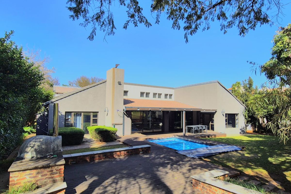 Rear view of the property featuring a swimming pool, timber decking, and a built-in brick braai area set within a landscaped garden.