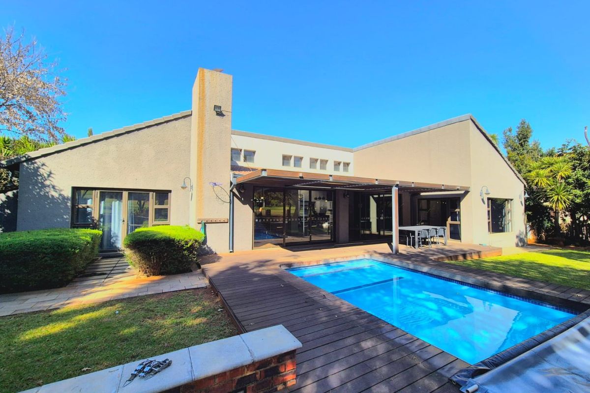 Rear exterior view featuring a swimming pool, timber decking, and a covered patio area with sliding glass doors leading into the home.