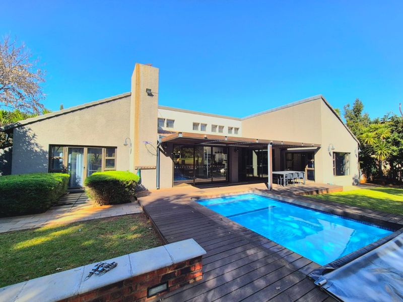 Rear exterior view featuring a swimming pool, timber decking, and a covered patio area with sliding glass doors leading into the home.