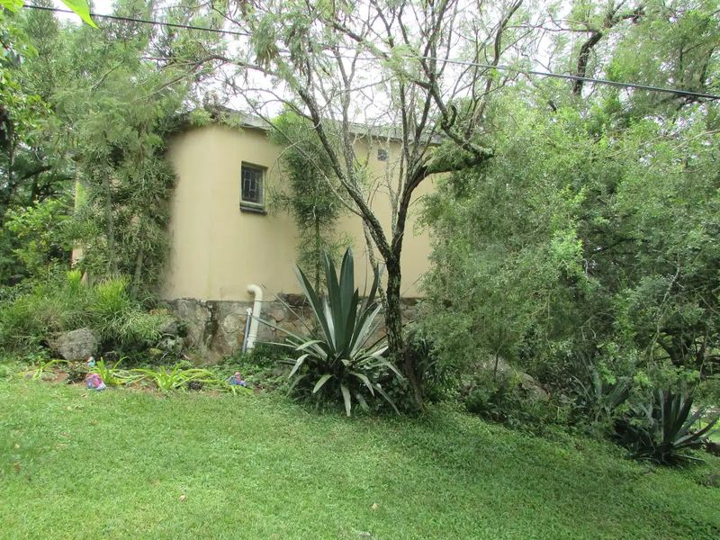 Rear view of the farm building featuring plastered masonry walls, a stone foundation, and surrounding mature trees and garden.