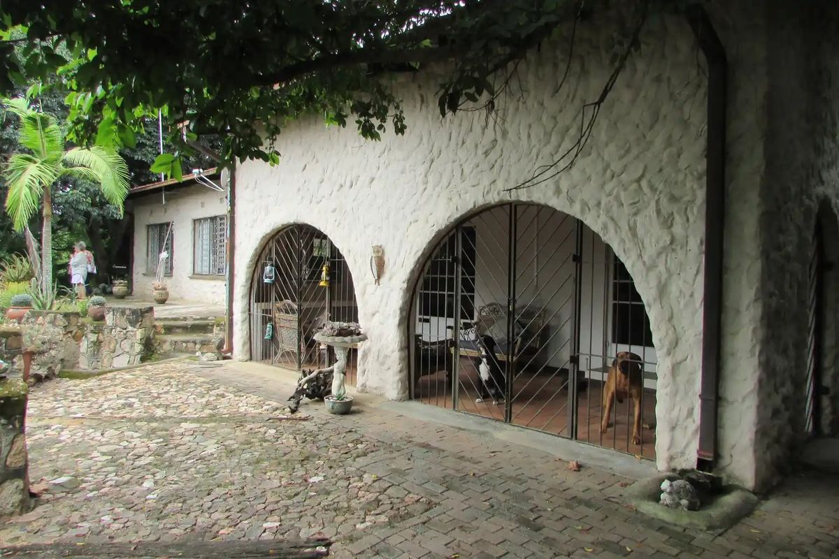 Covered patio area featuring distinctive stone masonry walls with arched openings and secure metal gates, overlooking a rustic cobblestone courtyard.