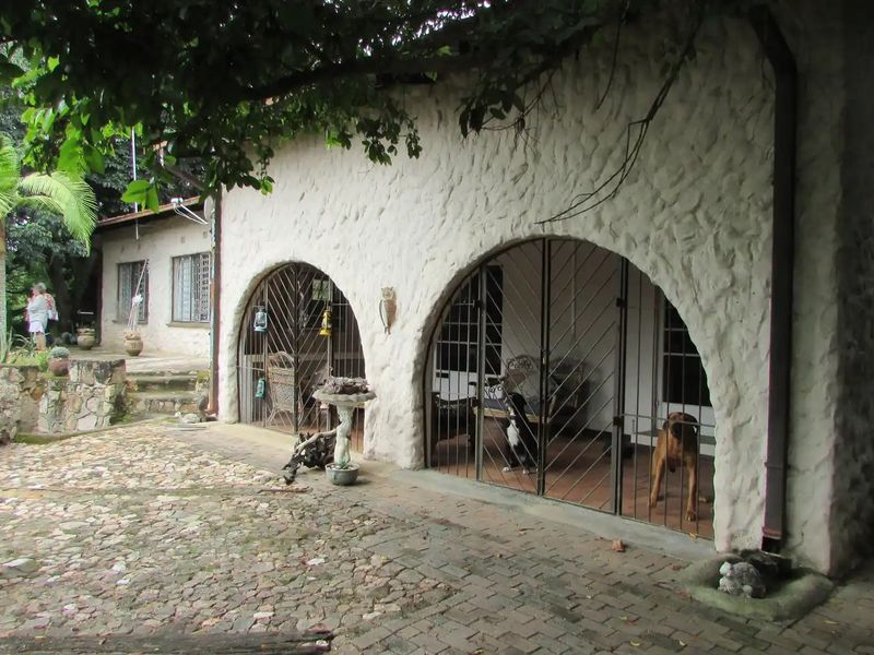 Covered patio area featuring distinctive stone masonry walls with arched openings and secure metal gates, overlooking a rustic cobblestone courtyard.
