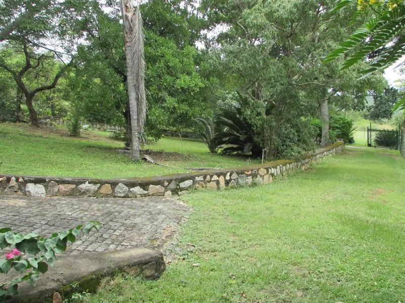 A spacious garden area featuring a stone retaining wall, cobblestone paving, and mature trees, providing a natural and established outdoor setting.
