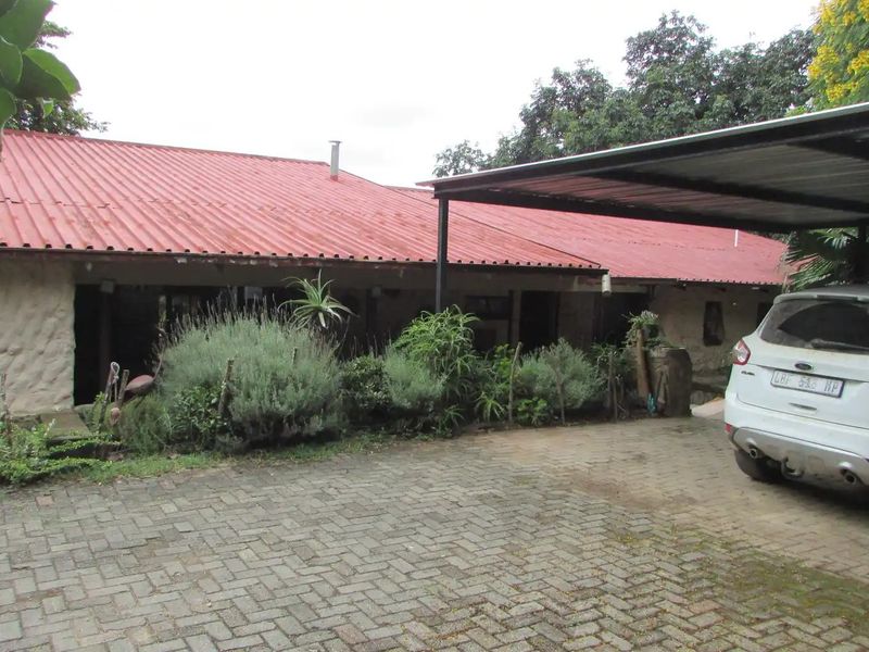 Front exterior view of a farm-style dwelling featuring stone masonry walls, a corrugated metal roof, and a paved driveway with an attached carport.