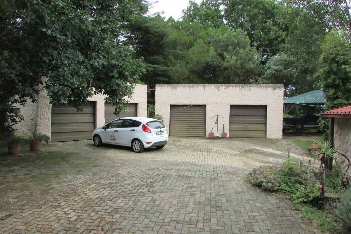 A four-car garage facility featuring a paved driveway and textured exterior walls, set within a mature garden environment.