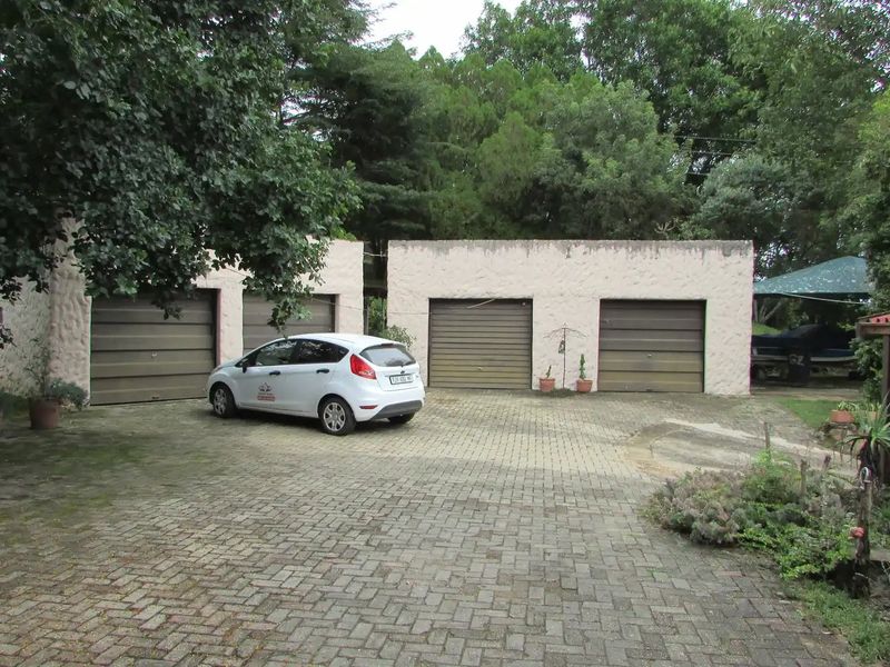 A four-car garage facility featuring a paved driveway and textured exterior walls, set within a mature garden environment.
