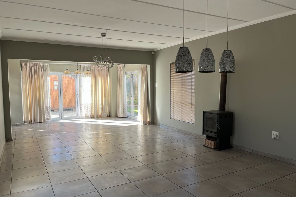 Spacious open-plan living area featuring neutral tiled flooring, a modern freestanding fireplace, and large sliding glass doors providing ample natural light.