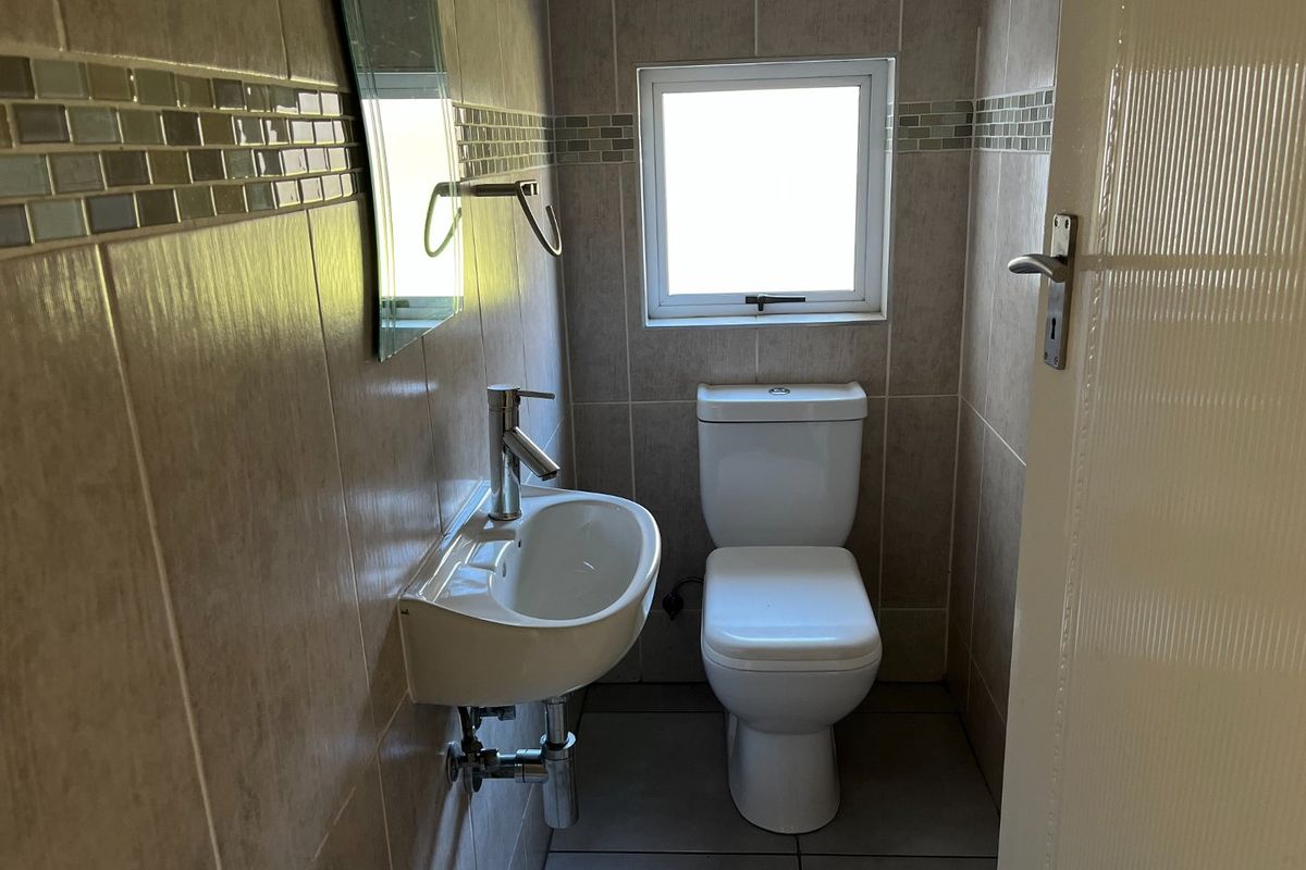 A compact guest bathroom featuring a wall-mounted basin, modern toilet, and neutral tiled walls with a decorative mosaic border.