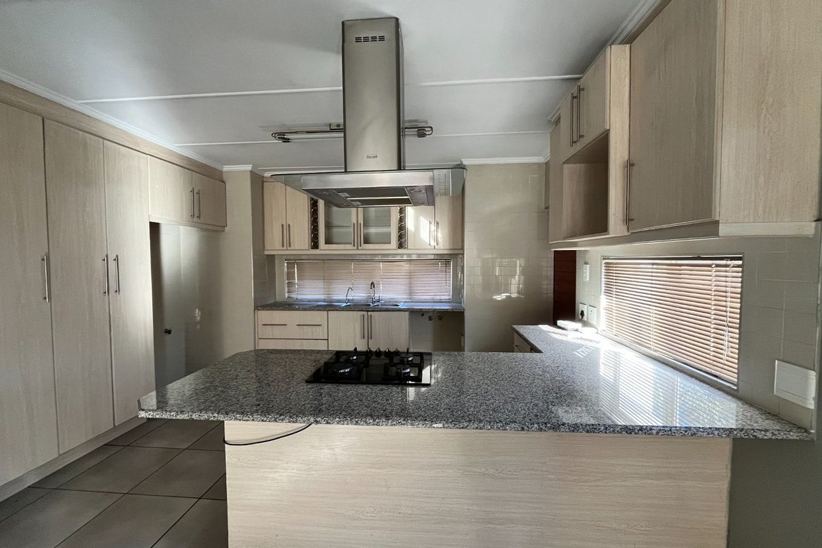 A spacious, modern kitchen featuring light wood cabinetry, granite countertops, a central island with a gas hob, and a stainless steel extractor fan.