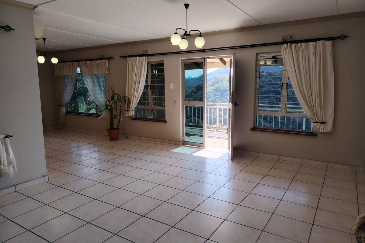 Spacious, light-filled living area featuring neutral tiled flooring, large windows with security bars, and direct access to an outdoor balcony with scenic views.