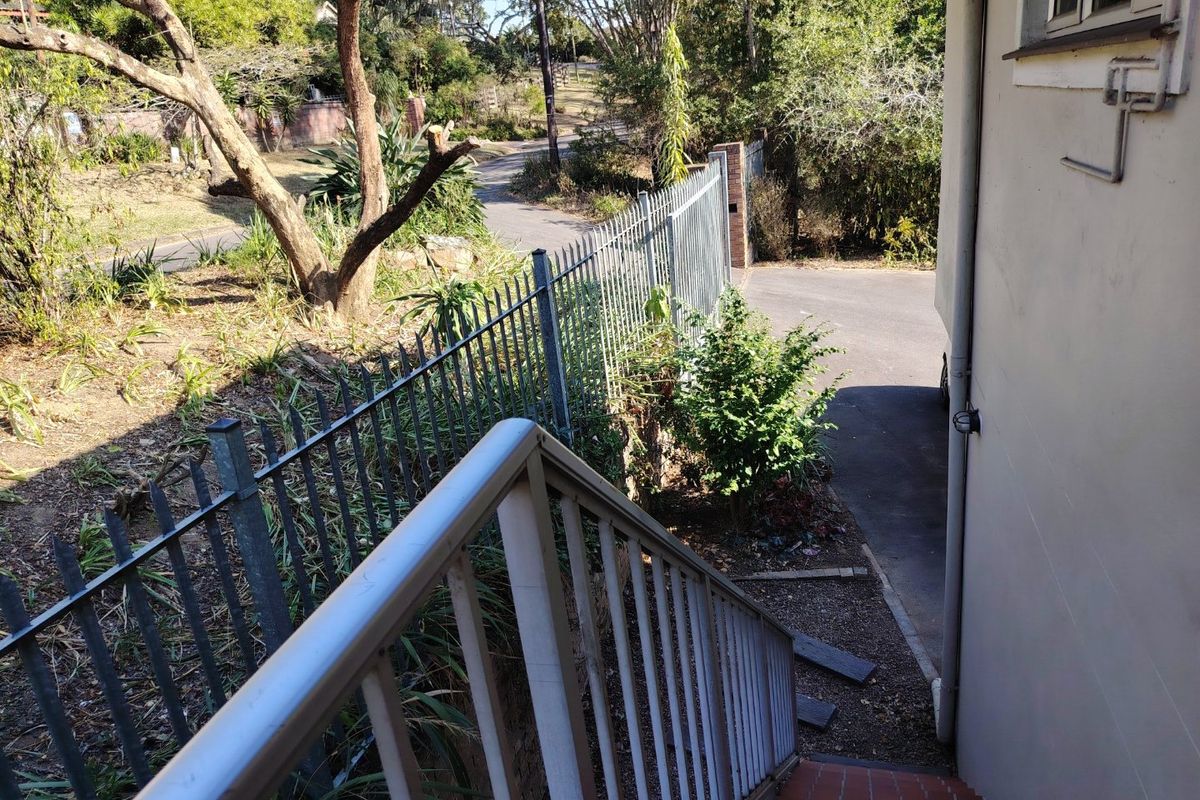 An exterior view of a rear staircase with metal handrails, leading down to a paved area enclosed by metal security fencing.