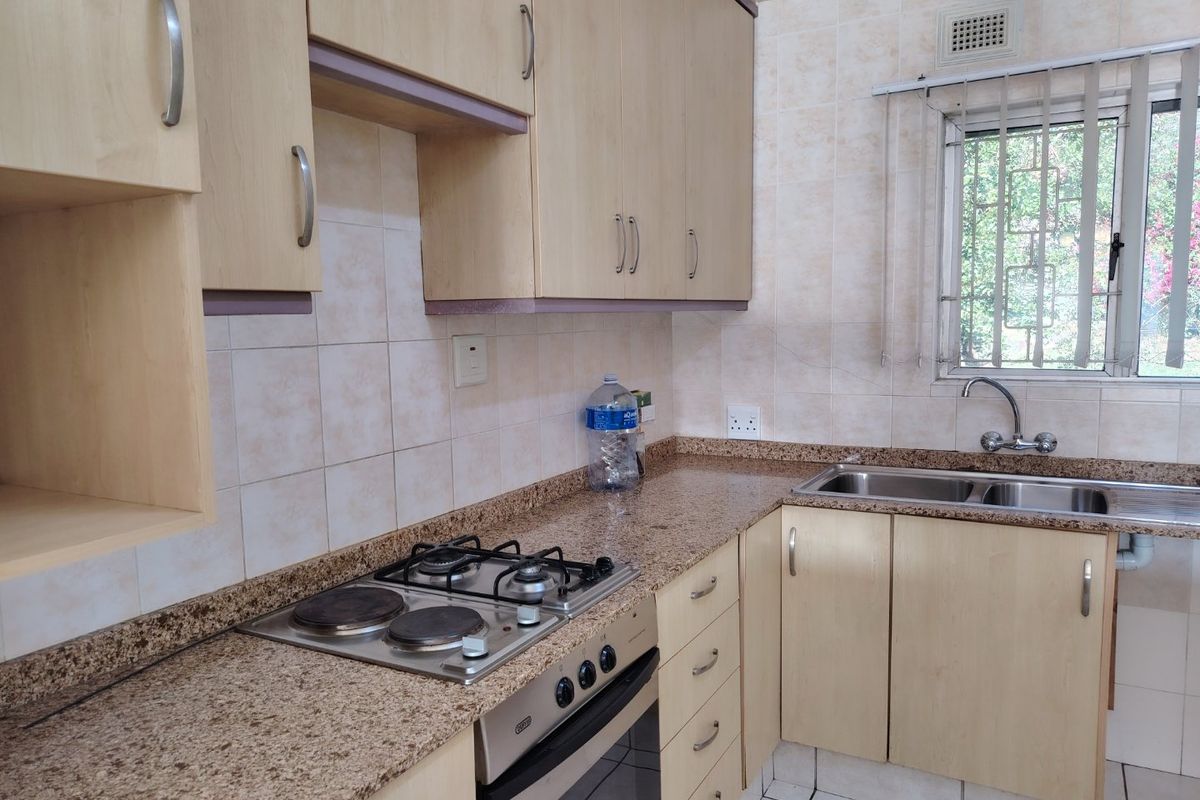 A functional kitchen featuring light wood cabinetry, granite countertops, a built-in oven with gas and electric hob, and tiled finishes throughout.