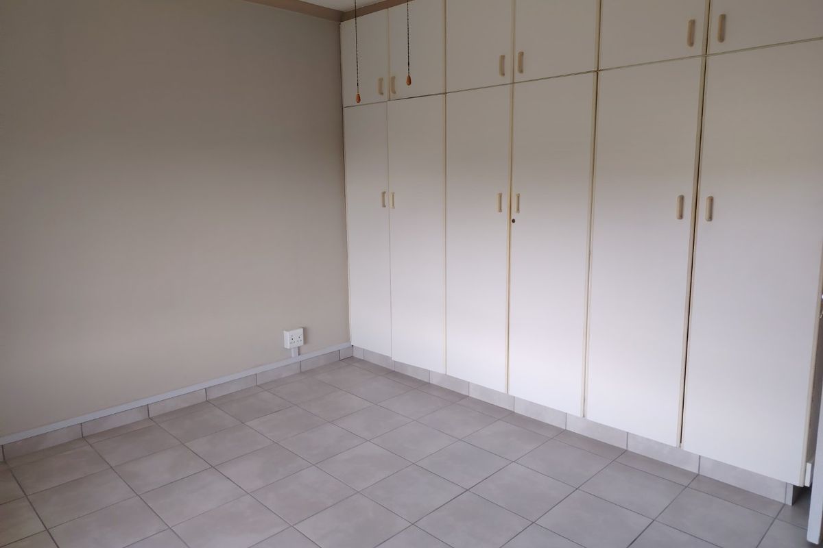 A clean, empty bedroom featuring neutral tiled flooring and extensive floor-to-ceiling built-in cupboards providing ample storage space.