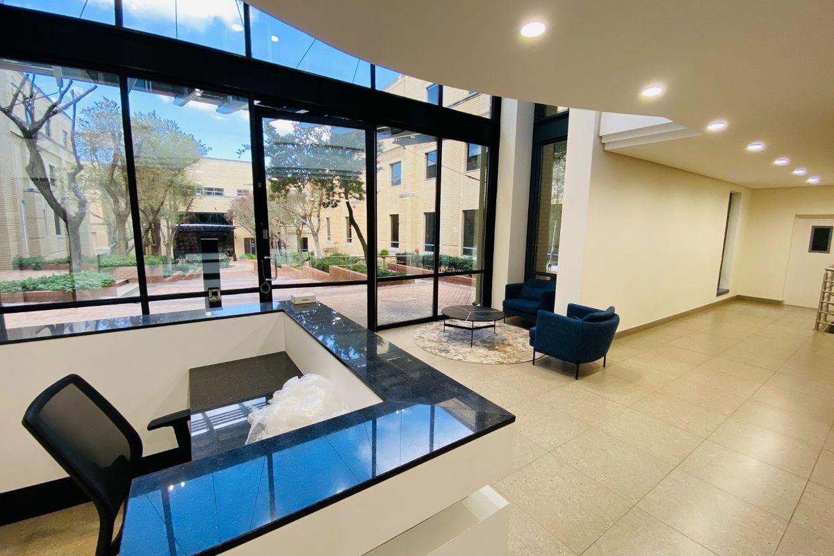 Modern commercial entrance lobby featuring a sleek reception desk, expansive floor-to-ceiling glass windows, and bright recessed lighting.
