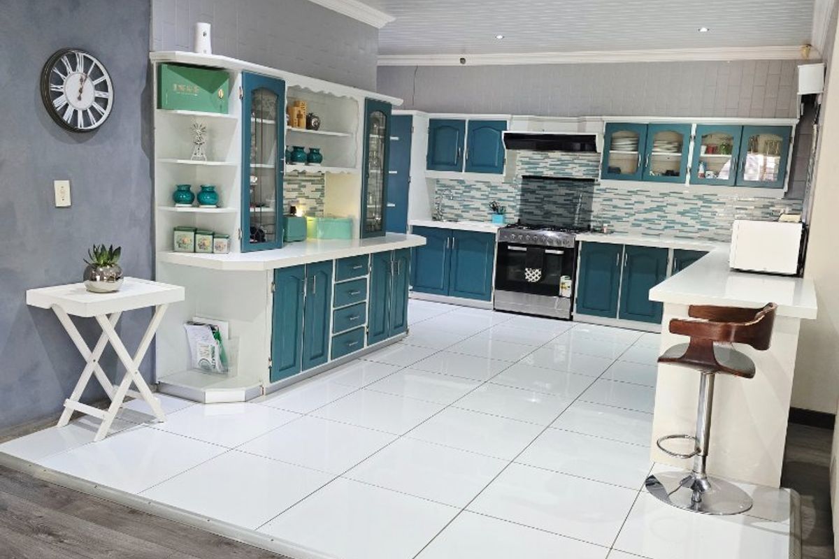 Spacious kitchen featuring teal cabinetry, a breakfast bar, gas stove with extractor, and modern tiled flooring, offering a functional and stylish cooking environment.