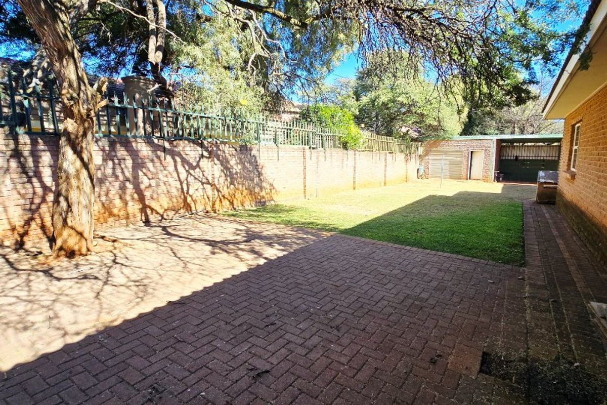 Spacious rear garden featuring brick paving, a well-maintained lawn, and a secure brick boundary wall with integrated metal fencing.