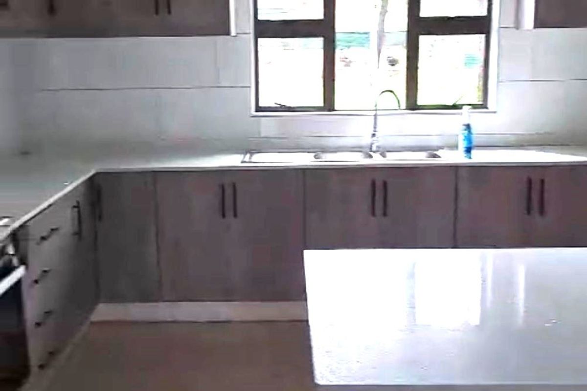 A modern kitchen featuring grey built-in cabinetry, stone countertops, a double basin sink, and tiled flooring with a central island.