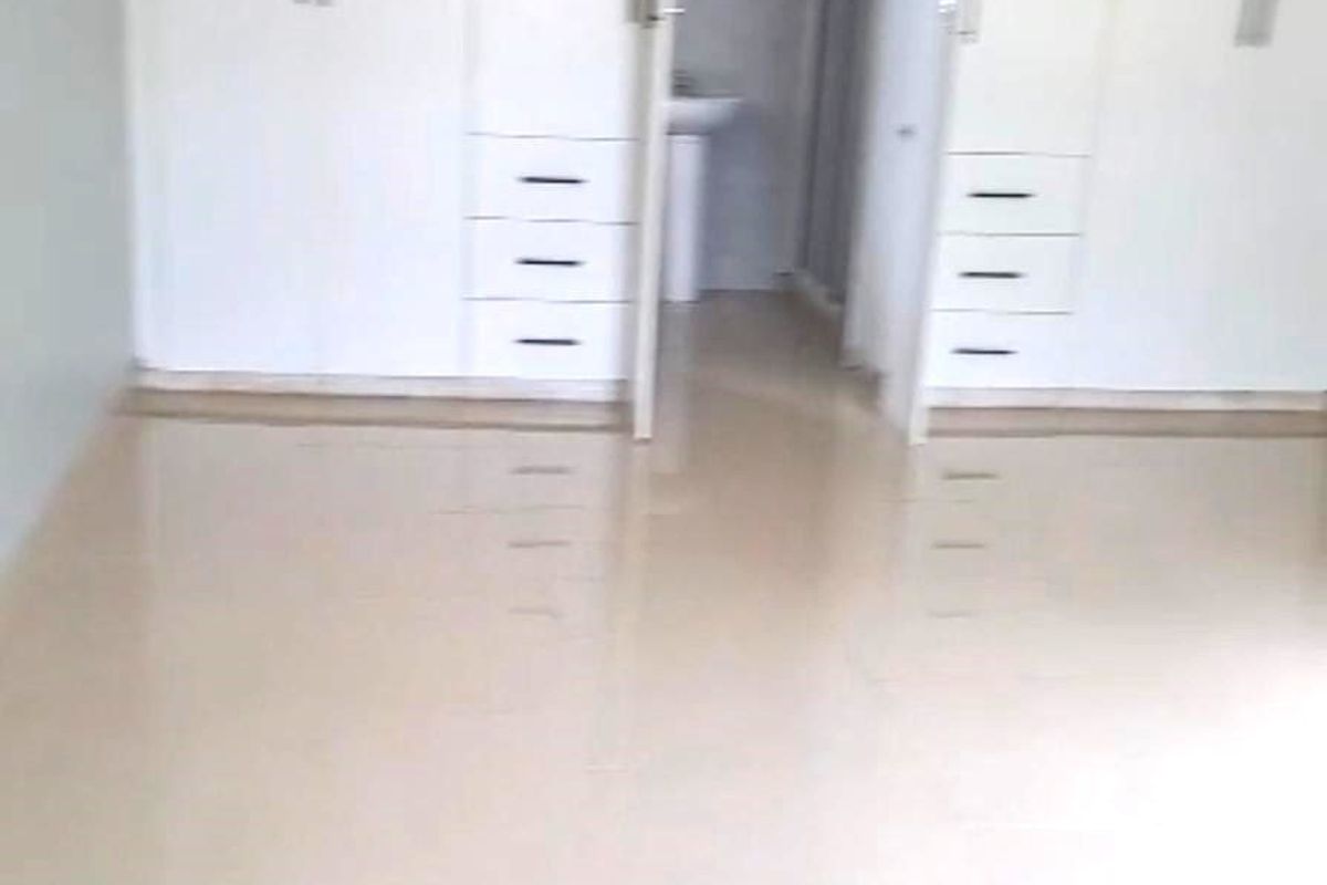 An empty bedroom featuring built-in cupboards, tiled flooring, and direct access to an en-suite bathroom.