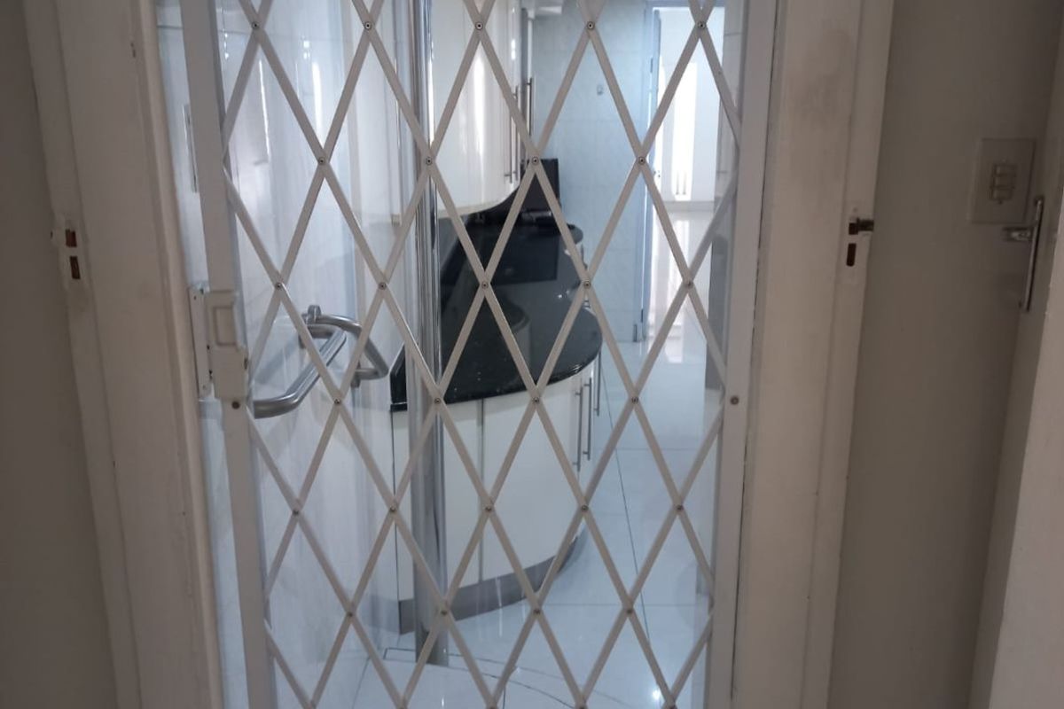 A kitchen viewed through a security gate, featuring tiled floors, built-in cabinetry, and stone countertops.