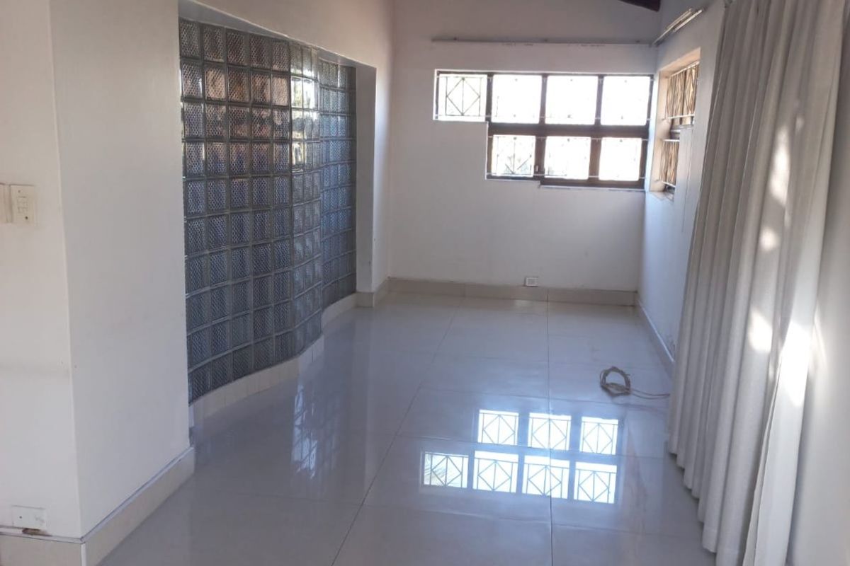 An empty living area featuring high exposed timber beam ceilings, polished floor tiles, and a unique glass block feature wall.
