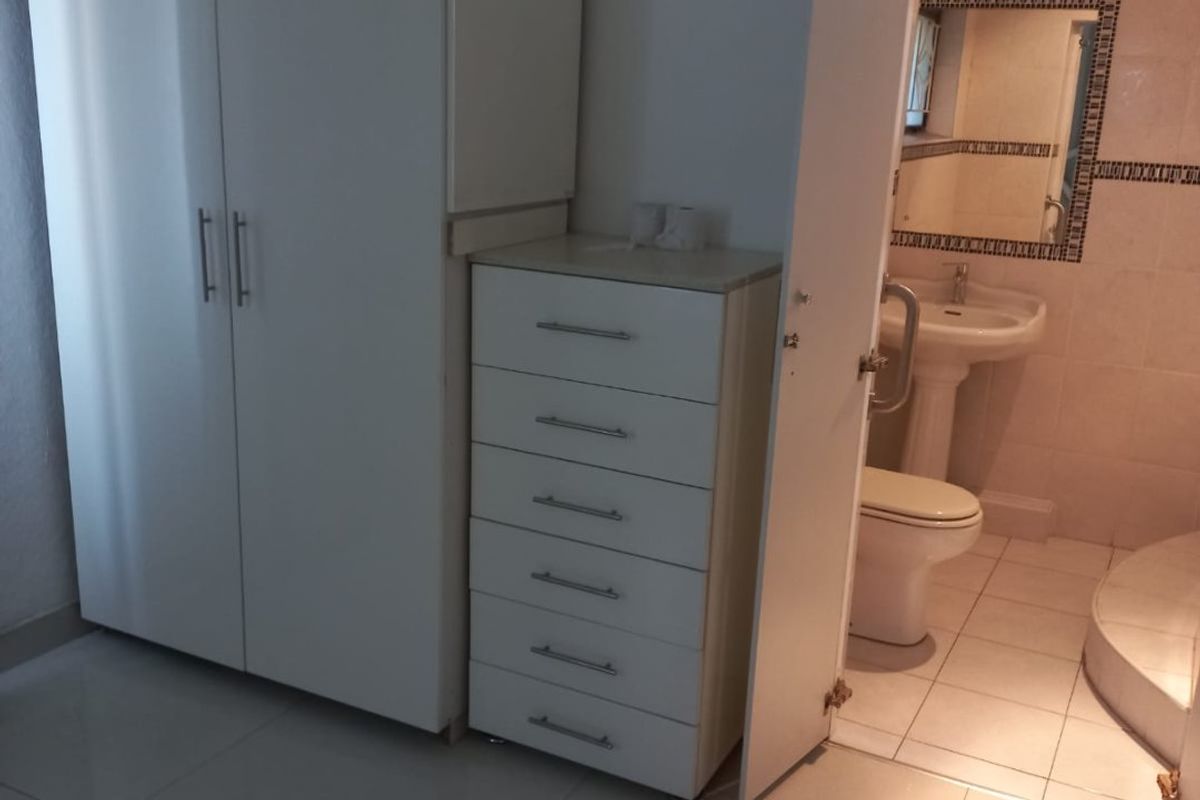 Bedroom featuring built-in wardrobes and tiled flooring, with direct access to an en-suite bathroom equipped with a pedestal basin and shower.