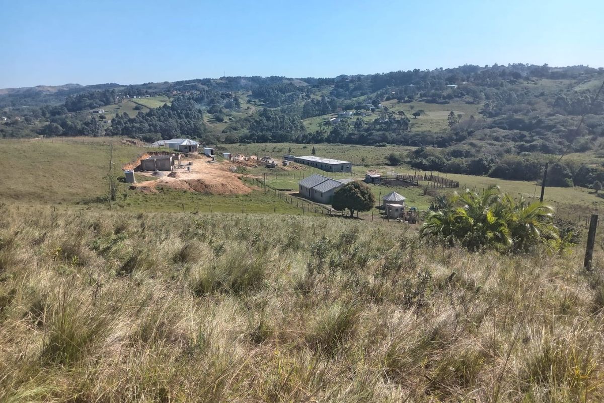 An elevated view of a large residential plot featuring rolling hills, open grassland, and existing outbuildings in a rural setting.