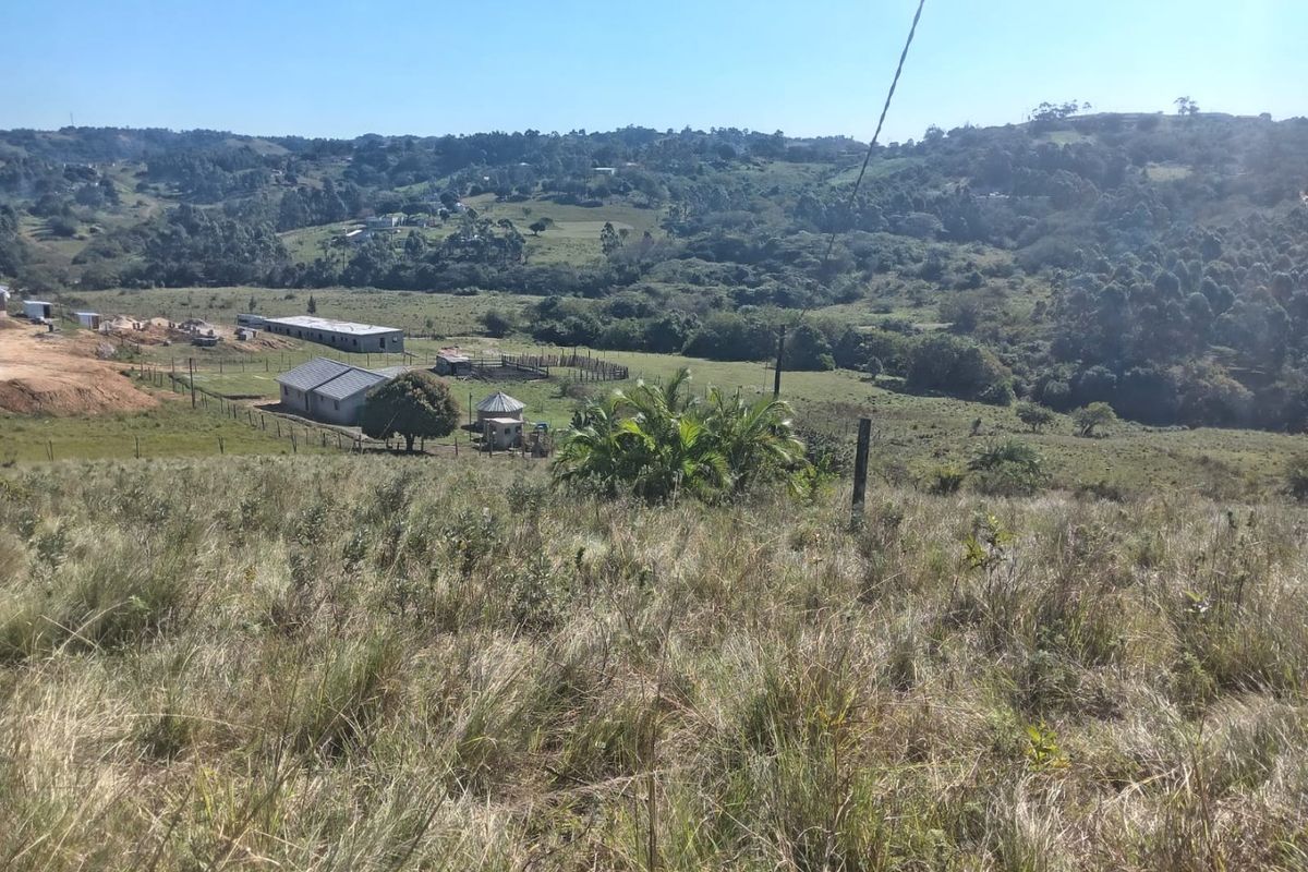 Expansive elevated view overlooking a rural landscape with rolling hills, natural vegetation, and existing small structures in the distance.