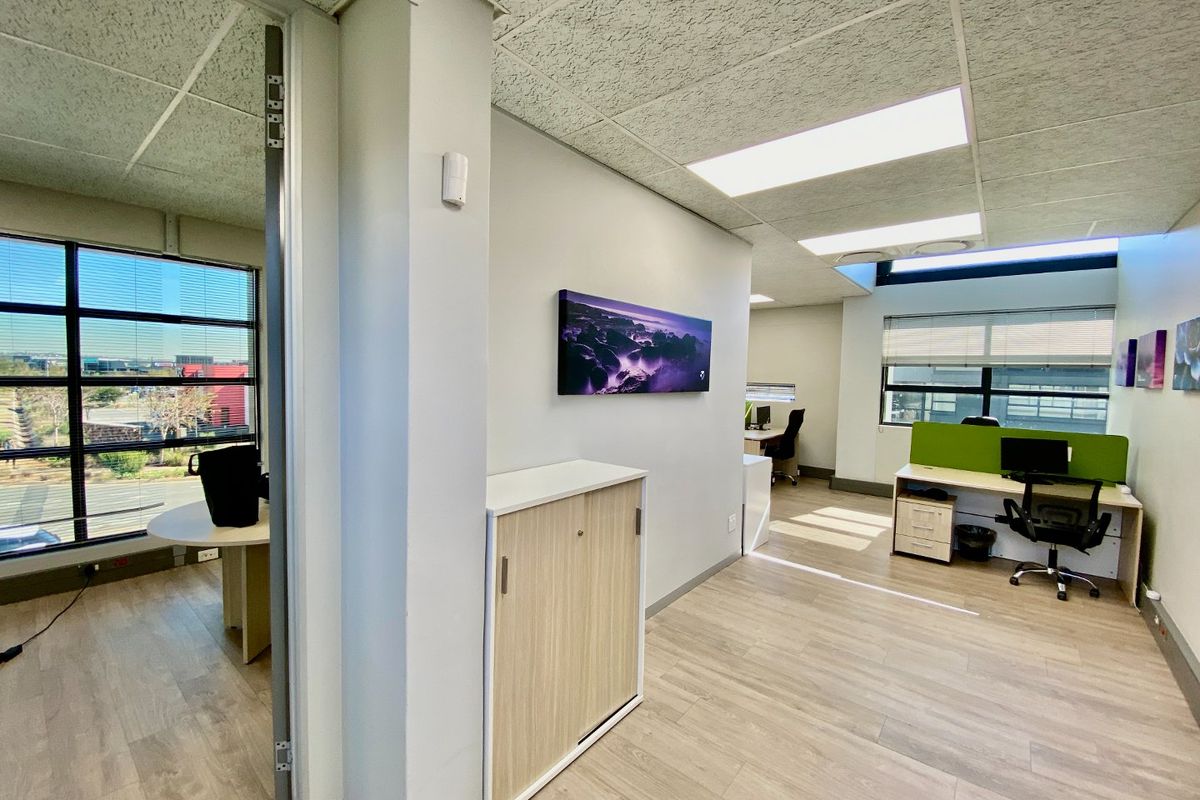 Modern commercial office space featuring laminate flooring, suspended ceilings with recessed lighting, and large windows providing ample natural light.