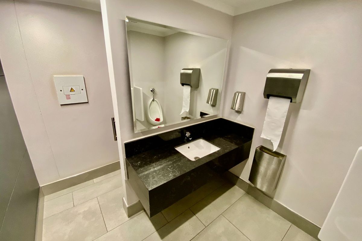 A clean, modern commercial restroom featuring a wall-mounted vanity with stone countertop, integrated sink, mirror, and stainless steel fixtures.