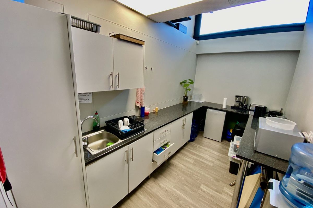 A functional commercial kitchenette featuring white cabinetry, dark granite countertops, a stainless steel sink, and durable vinyl flooring.