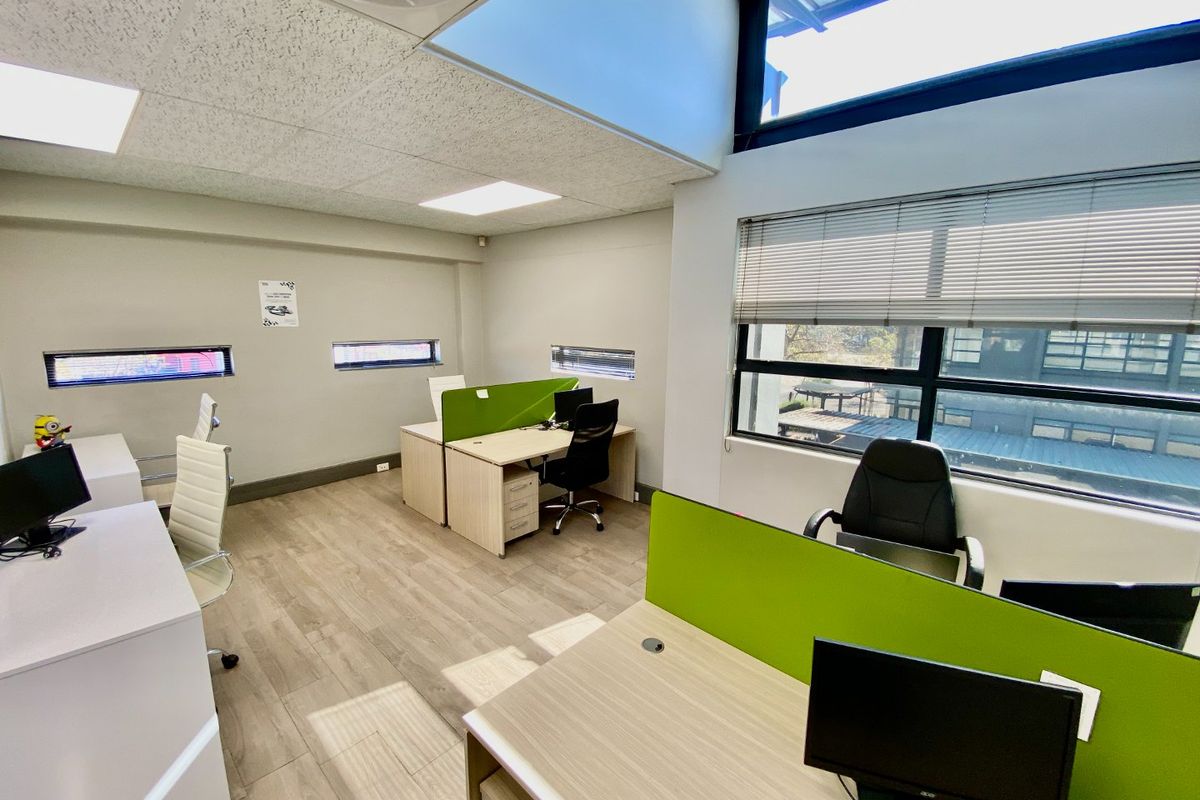 Modern commercial office space featuring wood-look flooring, suspended ceilings with recessed lighting, and large windows providing ample natural light.