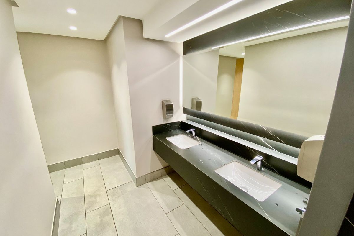 Modern commercial bathroom featuring a sleek double vanity with stone countertop, undermount sinks, and integrated mirror lighting.