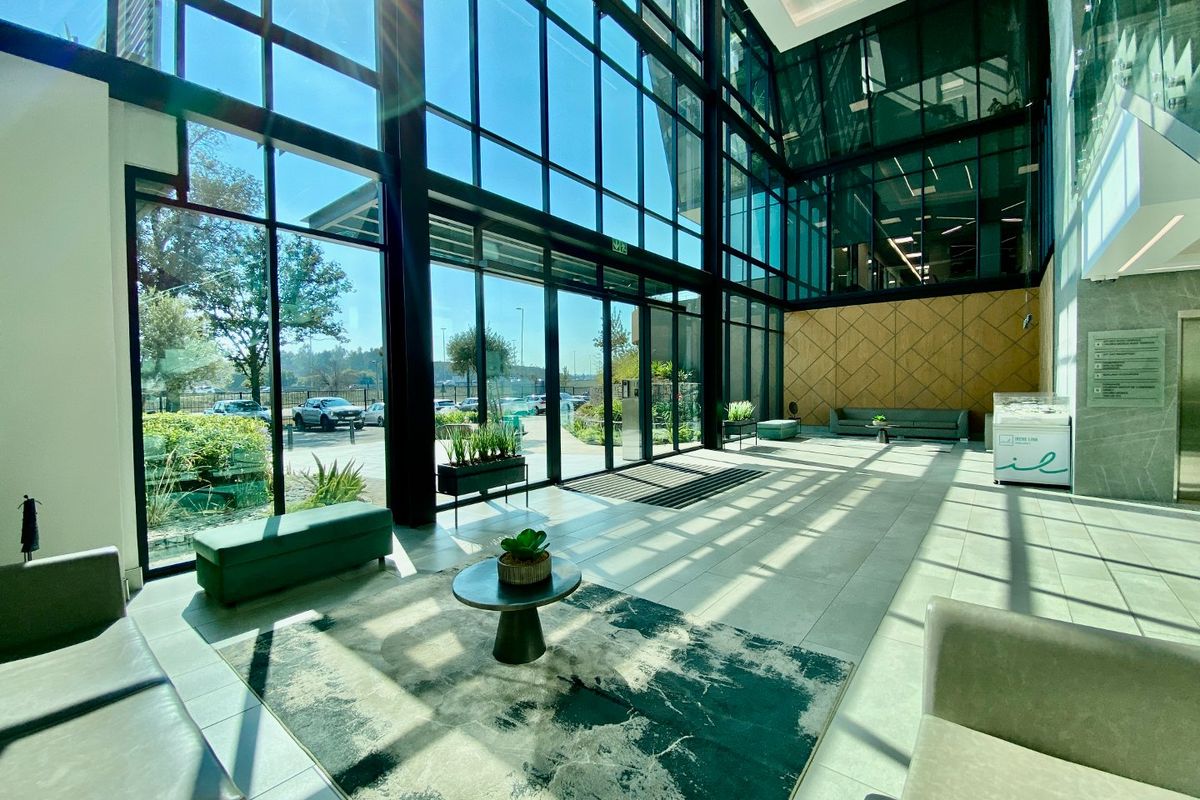 Modern commercial building entrance lobby featuring expansive floor-to-ceiling glass windows, tiled flooring, and contemporary timber wall paneling.