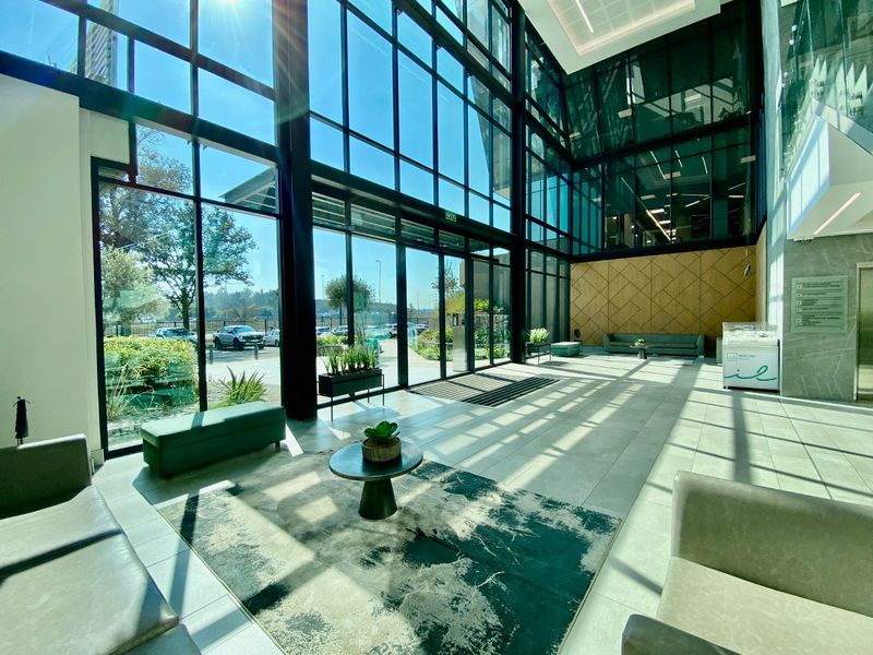 Modern commercial building entrance lobby featuring expansive floor-to-ceiling glass windows, tiled flooring, and contemporary timber wall paneling.