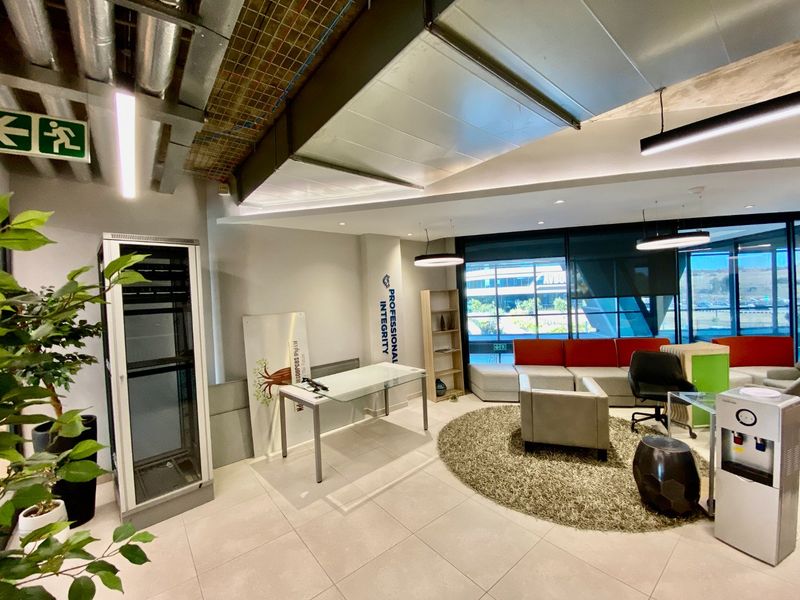 Modern commercial office space featuring exposed industrial ceiling ducting, tiled flooring, and large windows providing ample natural light.