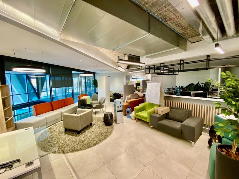 Spacious open-plan commercial office area featuring modern tiled floors, exposed industrial ceiling ducting, and expansive floor-to-ceiling glass windows providing ample natural light.
