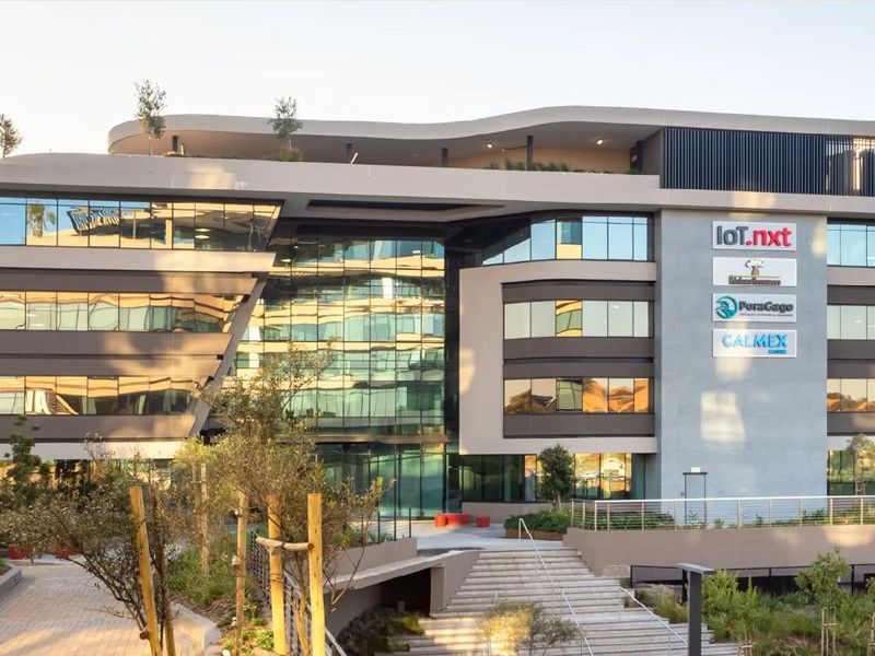 Modern commercial office building featuring a contemporary glass facade, integrated corporate signage, and professionally landscaped terraced grounds with pedestrian access.