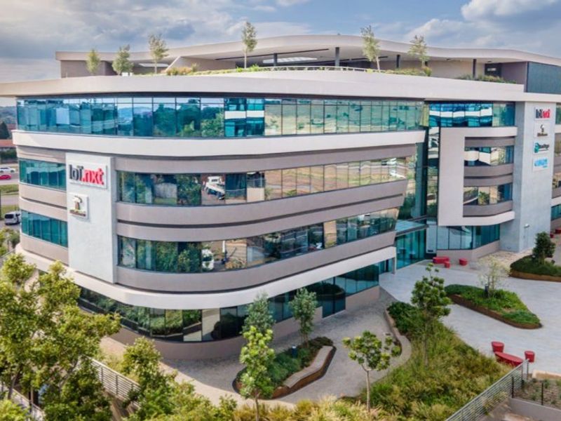 Aerial view of a modern multi-story commercial office building featuring a glass facade, landscaped courtyard, and rooftop terrace area.