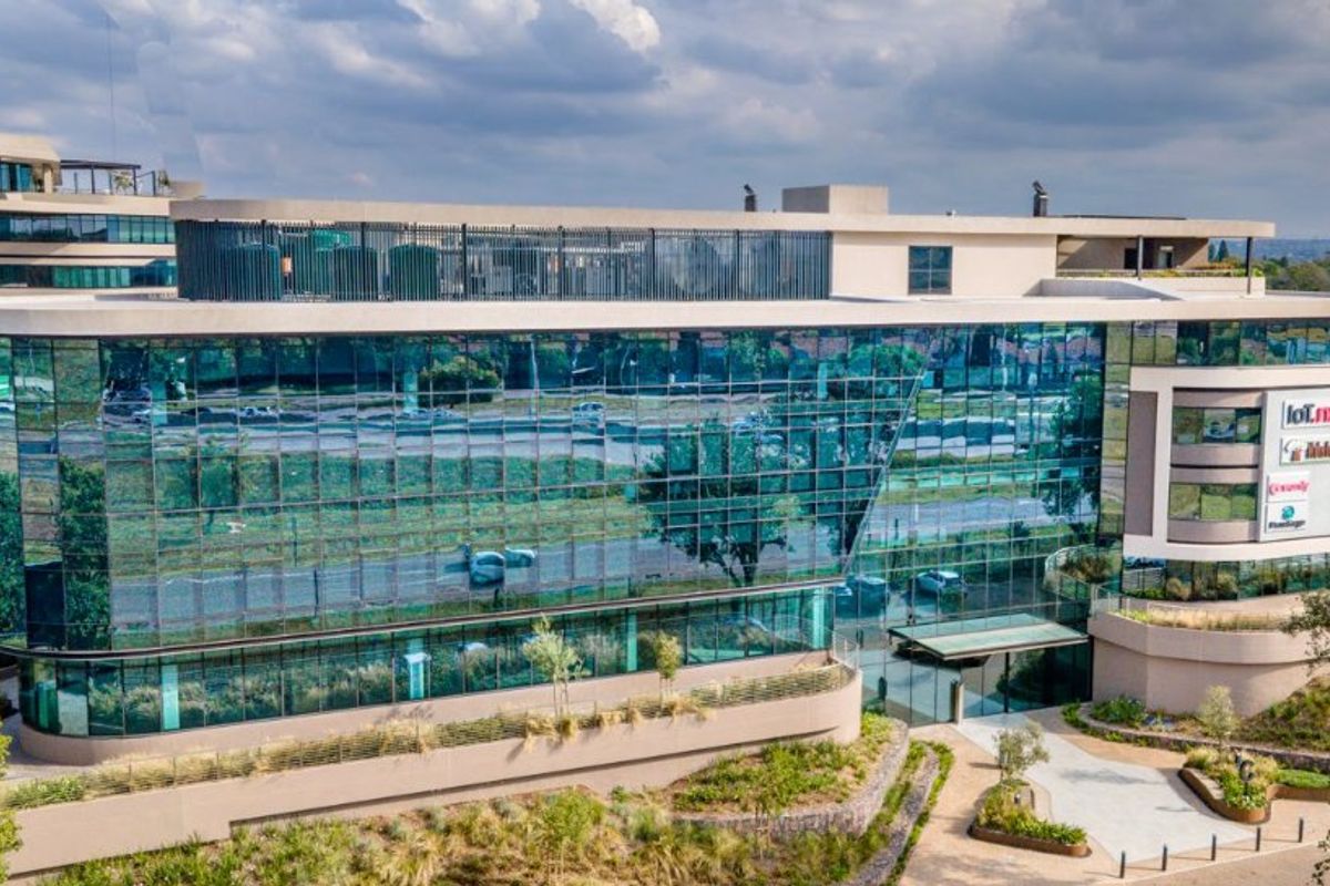 Aerial view of a modern commercial office building featuring extensive glass curtain walling, landscaped surroundings, and a prominent entrance area.