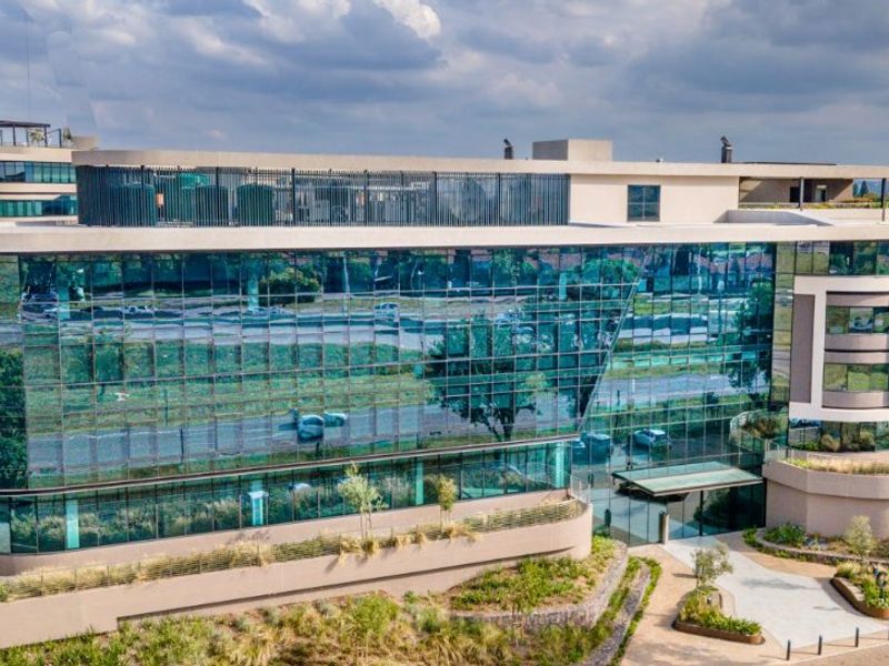 Aerial view of a modern commercial office building featuring extensive glass curtain walling, landscaped surroundings, and a prominent entrance area.