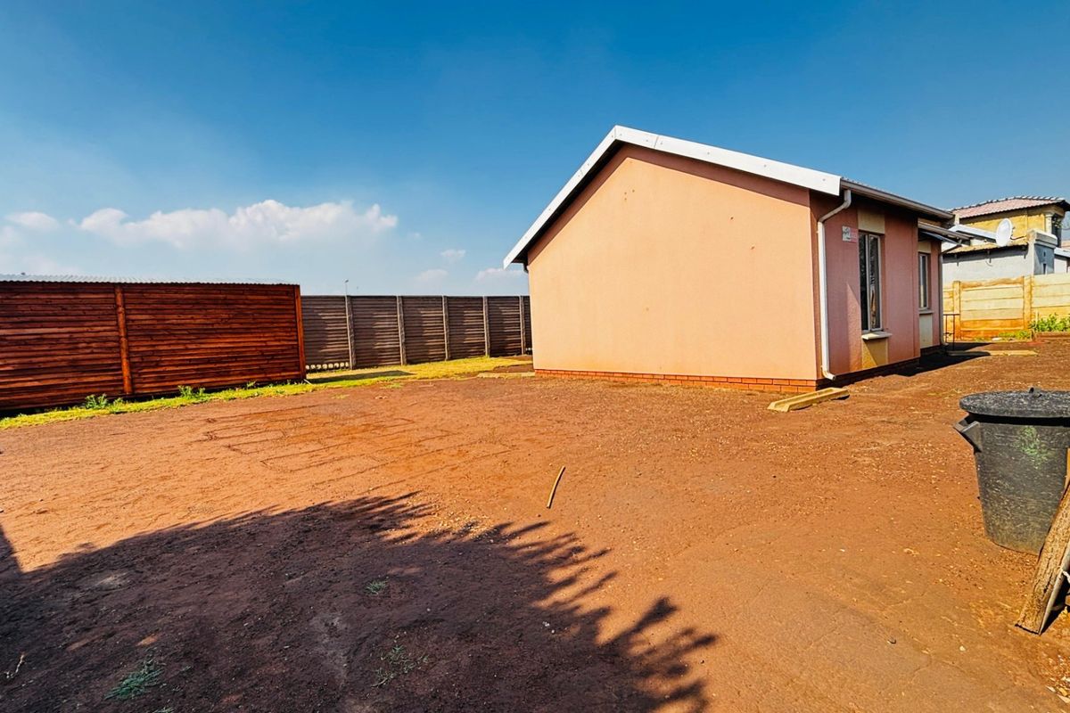Rear view of the property showing the side elevation, timber fencing, and an expansive unlandscaped yard area.